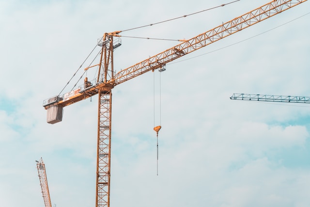 An upward shot of a yellow crane positioned hight in the sky, with two of cranes partly in view.