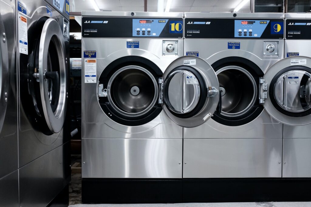 Multiple commercial washing machines with two open machines primarily in focus, inside a laundrette.