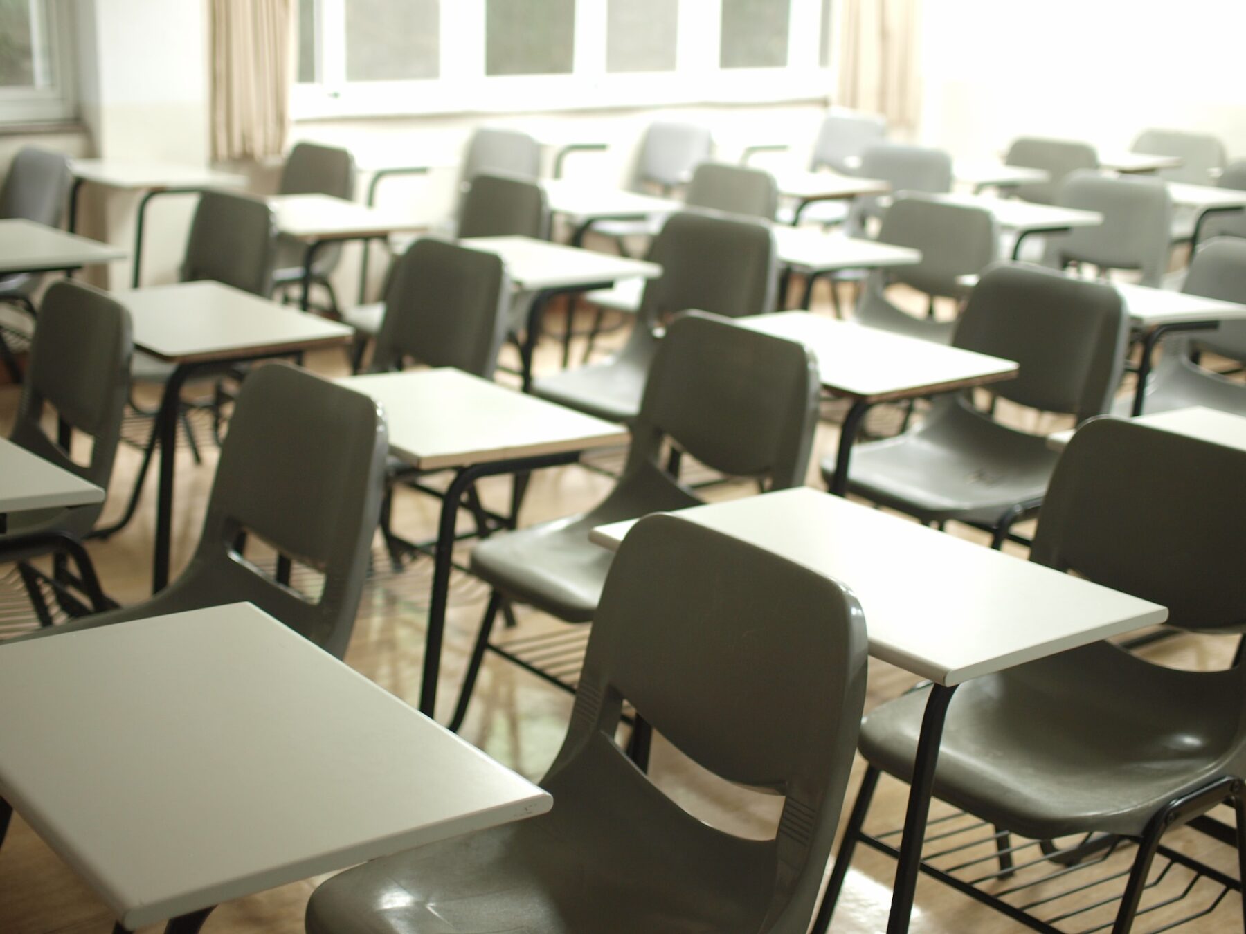 A empty classroom with desks and tables positioned consistently apart from one another.