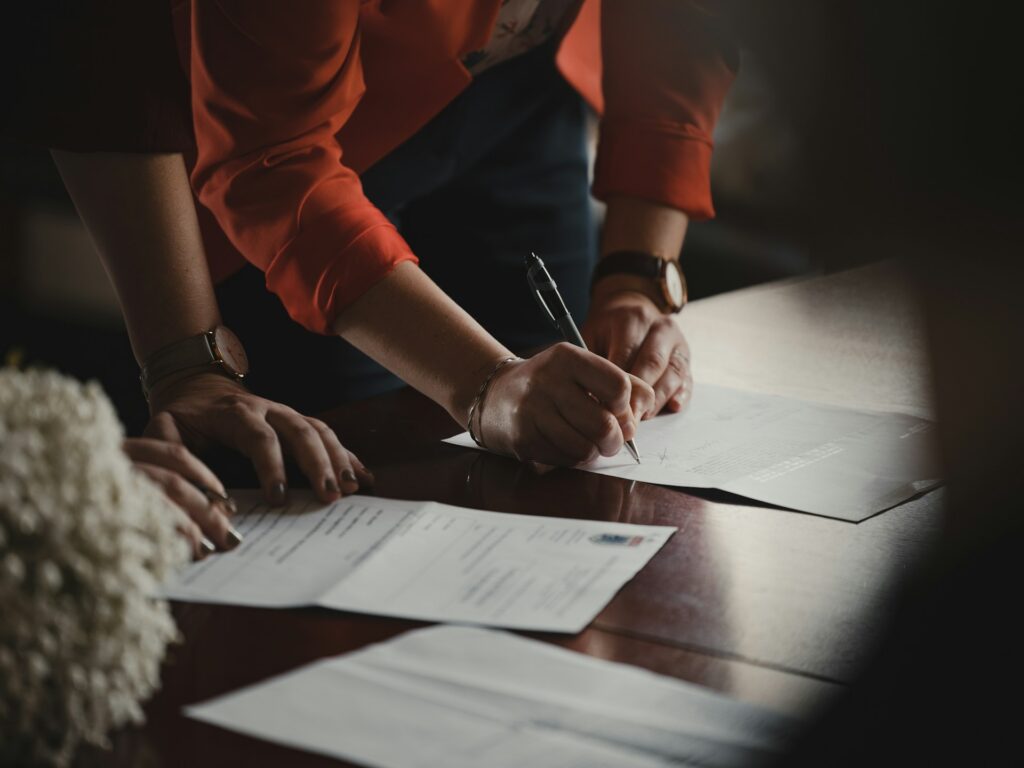 Two people standing over a table, signing paper documents.